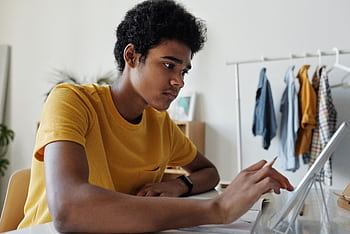 Teenage boy engaged in online learning using a tablet indoors. HD wallpaper