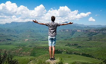 A man stands triumphantly with arms open, overlooking a scenic mountain range. HD wallpaper