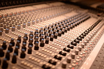 Detailed view of an analog audio mixing console with various knobs and sliders in a sound studio. HD wallpaper