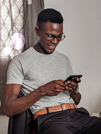 A happy young man uses his smart while sitting indoors, expressing joy. HD phone wallpaper