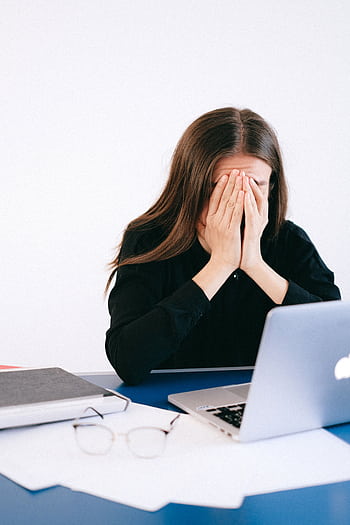A woman covers her face with hands in stress sitting at an office with a laptop and papers. HD phone wallpaper