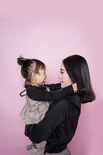 A happy mother holding her smiling daughter against a pink backdrop, showcasing love and togetherness. HD phone wallpaper