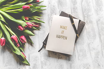 A notebook with 'Make It Happen' inscription beside a bouquet of pink tulips, capturing inspiration. HD wallpaper
