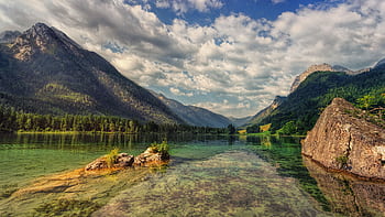 Serene view of a clear alpine lake surrounded by majestic mountains and lush forests under a cloudy sky. HD wallpaper