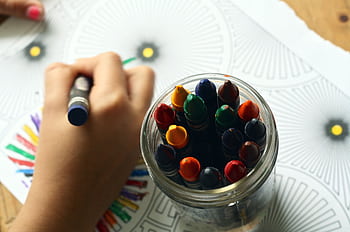 A child drawing with colorful crayons, fostering creativity and fun in a learning environment. HD wallpaper