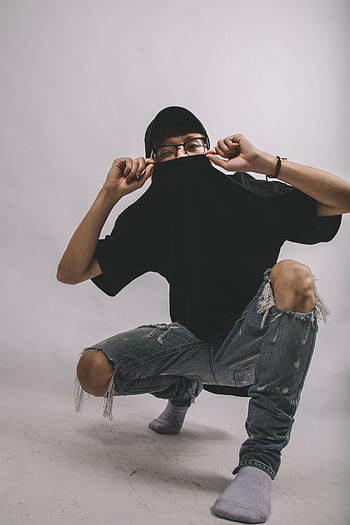 Stylish young adult posing with ripped jeans and cap in a studio setting. HD phone wallpaper