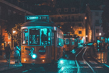 Illuminated vintage tram rides through Lisbon at night showcasing urban life and street lighting ambiance. HD wallpaper