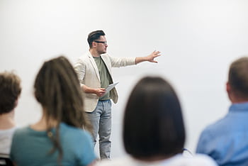 A man in a blazer gives a presentation to a captivated audience in a lecture setting. HD wallpaper