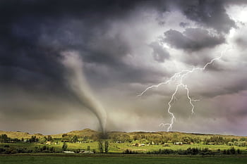 A powerful tornado and vibrant lightning striking over a rural countryside landscape. HD wallpaper