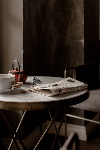 A cozy café setting with a teapot, teacup, and newspaper on a round table, inviting relaxation. HD phone wallpaper