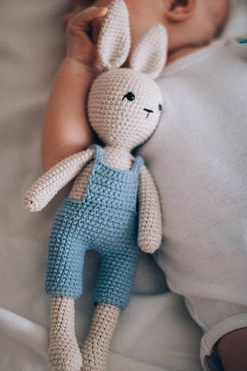 A cute baby lies next to a handmade crochet bunny doll in soft lighting. HD phone wallpaper