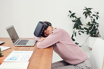 A woman wearing a VR headset rests on a desk beside a laptop, combining relaxation and technology. HD wallpaper