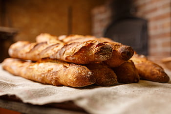 Warm, freshly baked rustic baguettes stacked in a cozy bakery setting. HD wallpaper