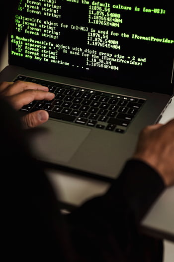 Close-up of hands typing code on a laptop in a dimly lit room, representing cybersecurity and hacking. HD phone wallpaper