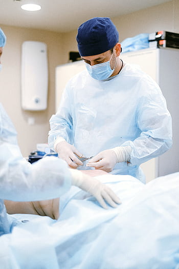 Doctors in protective gear performing surgery in a sterile operating room. HD phone wallpaper
