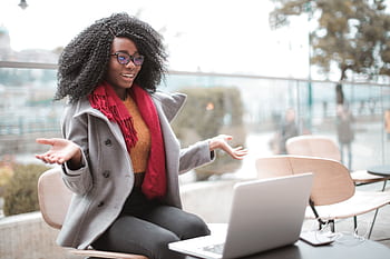 Smiling woman gesturing during a video call in a bright, modern café setting. HD wallpaper