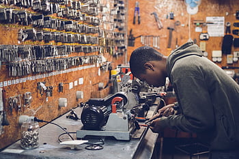 A focused craftsman works in a key-making workshop surrounded by tools and equipment. HD wallpaper