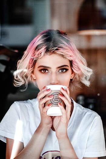 Portrait of a young woman with pink hair holding a cup in a cafe setting. HD phone wallpaper