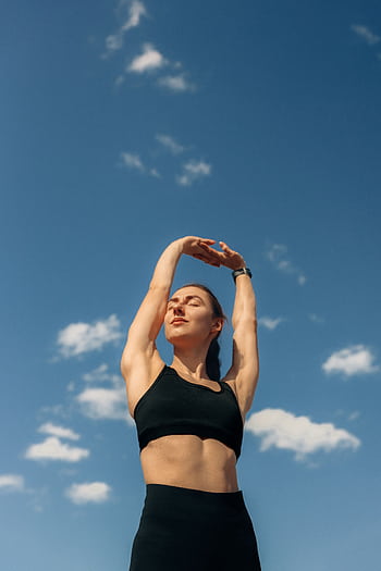 A woman in black leggings and sports bra stretches under a clear blue sky, promoting fitness and dom. HD phone wallpaper