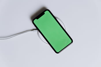 A minimalist smart with a green screen on a wireless charger, ideal for tech mockups. HD wallpaper