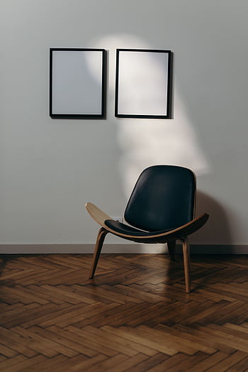 A modern armchair sits under two blank frames on an elegant wooden floor. HD phone wallpaper