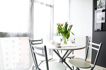Bright dining space with table, chairs, tulips, and natural light through large windows. HD wallpaper