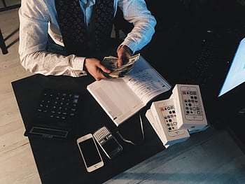 Businessman organizing finances with tech devices and cash on desk. HD wallpaper