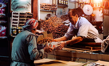 Two men exchanging dates in a vibrant Dubai spice market stall. HD wallpaper