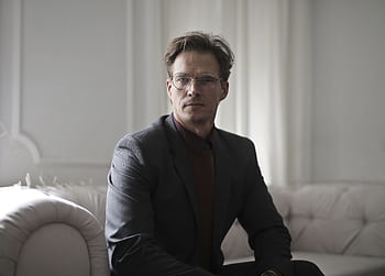 Professional man in a stylish suit sitting on a sofa in a luxuriously designed room. HD wallpaper