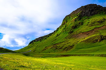 A vibrant landscape featuring a green mountain and blue sky with scattered clouds, perfect for nature lovers. HD wallpaper