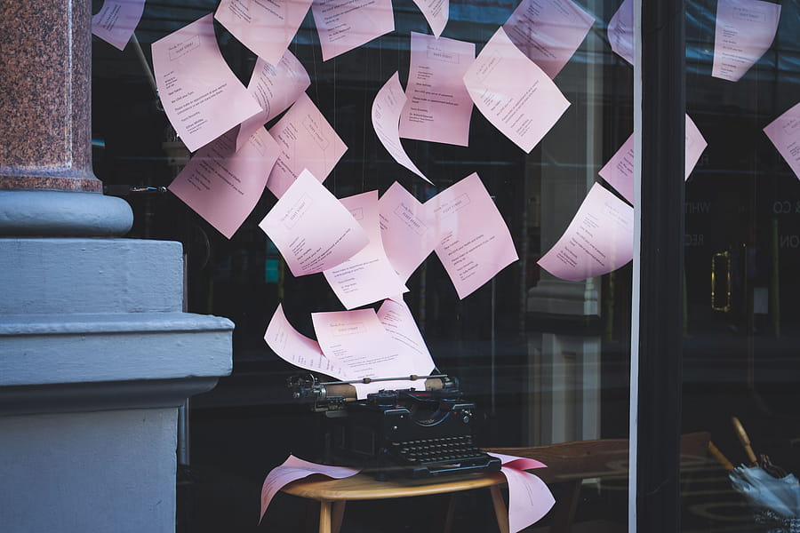 Artistic display of a vintage typewriter with pink papers floating in a window setting, indoors. HD wallpaper