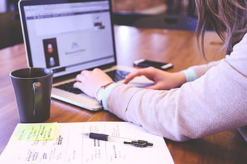 Businesswoman typing on laptop with notes and coffee on wooden desk. HD wallpaper