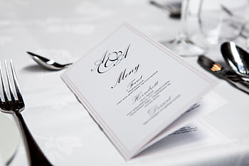 Close-up of a refined dining table with menu and silverware, showcasing elegance in a formal restaurant setting. HD wallpaper