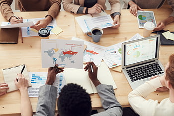 Diverse professionals brainstorming with laptops and charts in a contemporary office setting. HD wallpaper