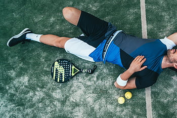 Tired young athlete resting on padel court with racket and balls nearby. HD wallpaper