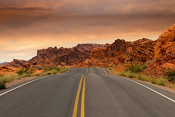A scenic highway winds through dramatic red desert rock formations under a colorful sunset sky. HD wallpaper