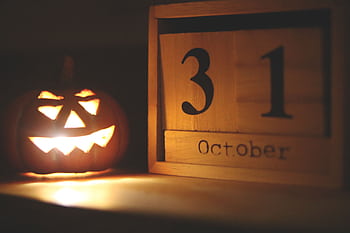 A glowing jack-o-lantern next to a calendar showing October 31, symbolizing Halloween celebration. HD wallpaper