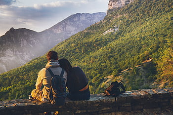 Couple sitting together enjoying a scenic mountain view at sunset, embodying love and adventure. HD wallpaper