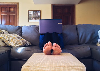 Person relaxing on a cozy couch with a laptop, embodying modern home comfort. HD wallpaper