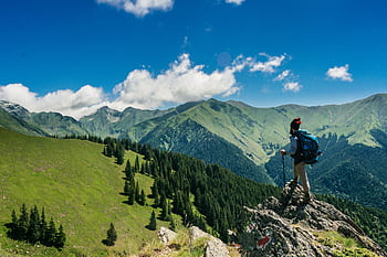 Adventurous hiker enjoying breathtaking views of lush green mountains in Romania under a clear blue sky. HD wallpaper