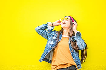 Smiling woman in sunglasses stands against vibrant yellow wall, radiating happiness. HD wallpaper