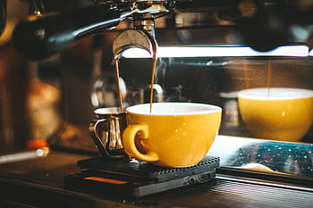 Steaming espresso pours into a yellow cup in a cozy café. HD wallpaper