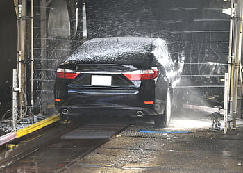 A black car being cleaned in an automated car wash with water and foam. HD wallpaper
