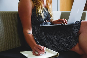 A woman multitasking with a laptop and writing notes, highlighting remote work and study. HD wallpaper