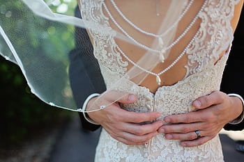 Close-up of bride and groom's embrace highlighting elegant lace bridal gown and pearl jewelry. HD wallpaper