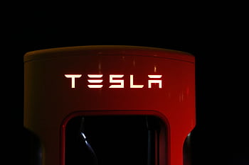 Close-up of a Tesla charging station illuminated at night, showcasing modern automotive technology. HD wallpaper