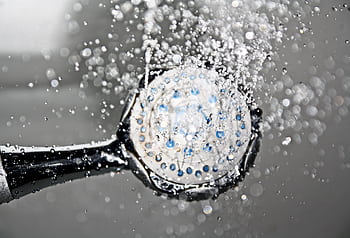 Close-up of a shower head releasing water droplets, creating a crisp and refreshing bathroom scene. HD wallpaper