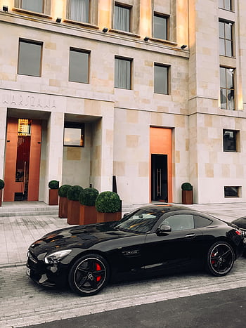 Black sports car parked in front of a modern building, highlighting urban elegance and sophisticated design. HD phone wallpaper
