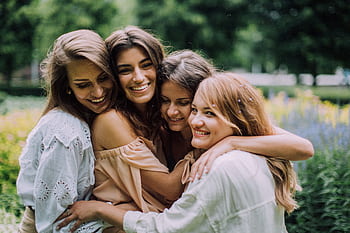 Four smiling women joyfully embrace in a lush green park during summer, showcasing genuine friendship and happiness. HD wallpaper
