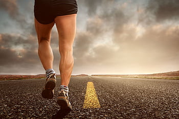 Runner's legs on a road during a sunset, symbolizing endurance and outdoor fitness training. HD wallpaper